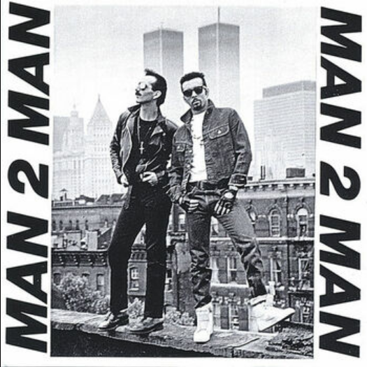 The sleeve for a "Man 2 Man" single, likely "Male Stripper". Man 2 Man pose in leather and denim on the edge of a rooftop in what looks like New York - the Twin Towers are conspicuous in the background - giving off gay vibes of the period.